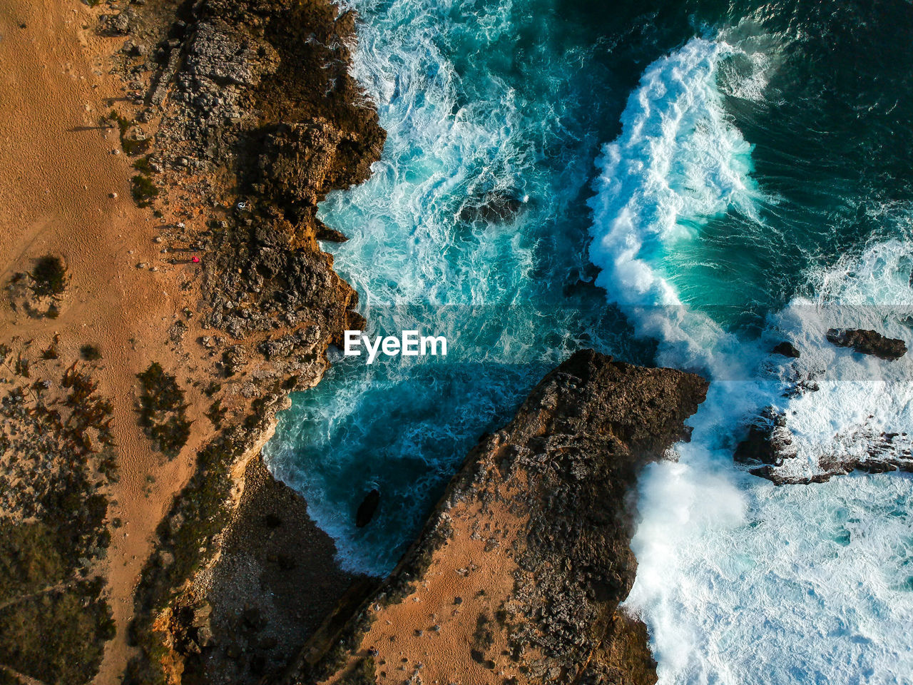 Aerial top view of sea waves hitting rocks on the beach with turquoise