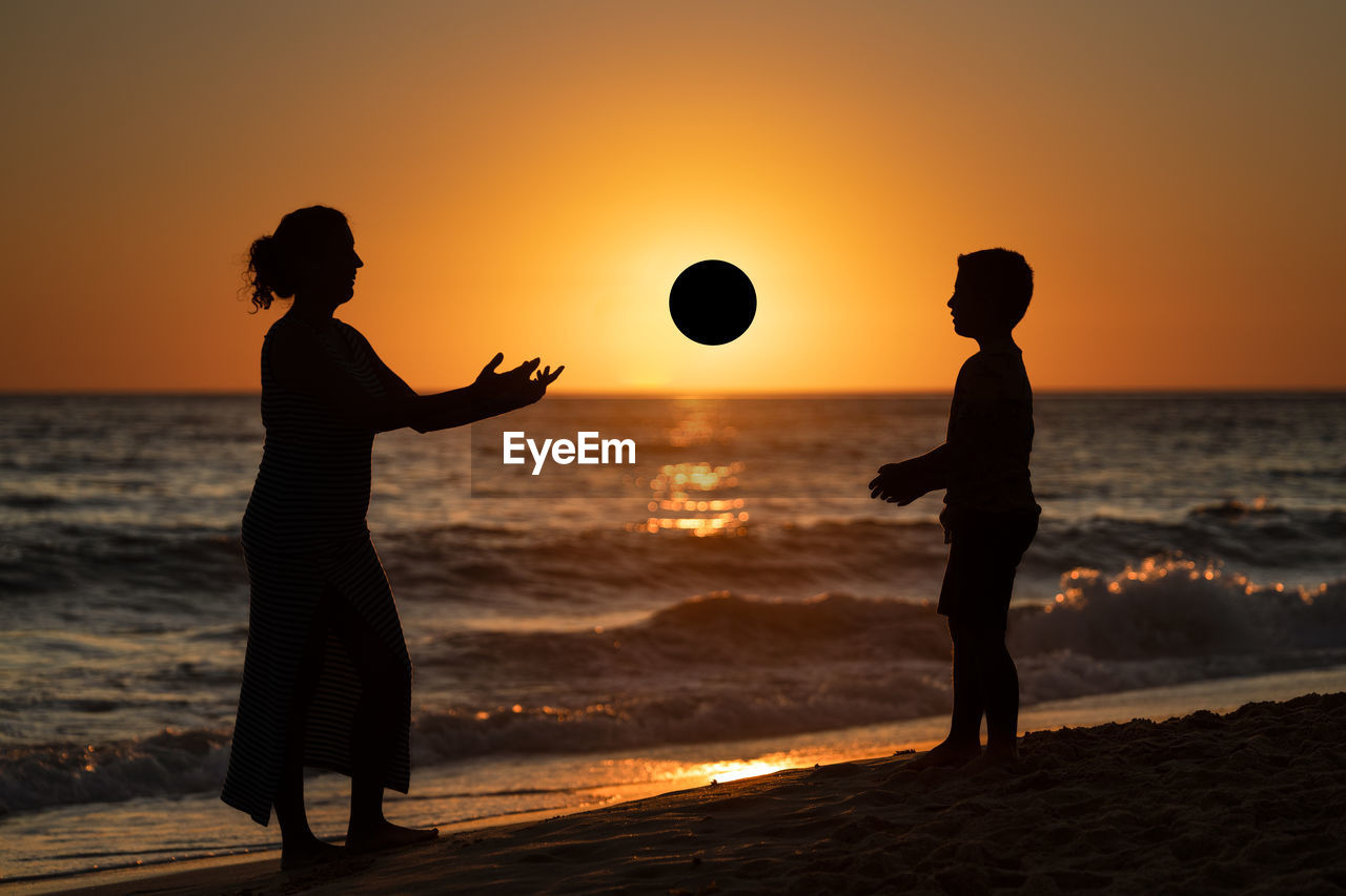 Mother and son playing with a ball on the beach at sunset