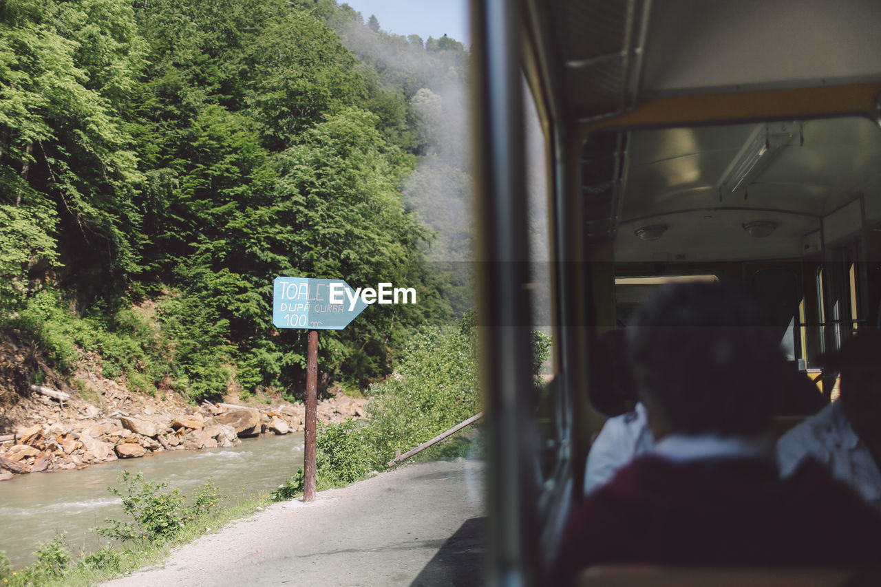 Passengers traveling in train by information sign at riverbank