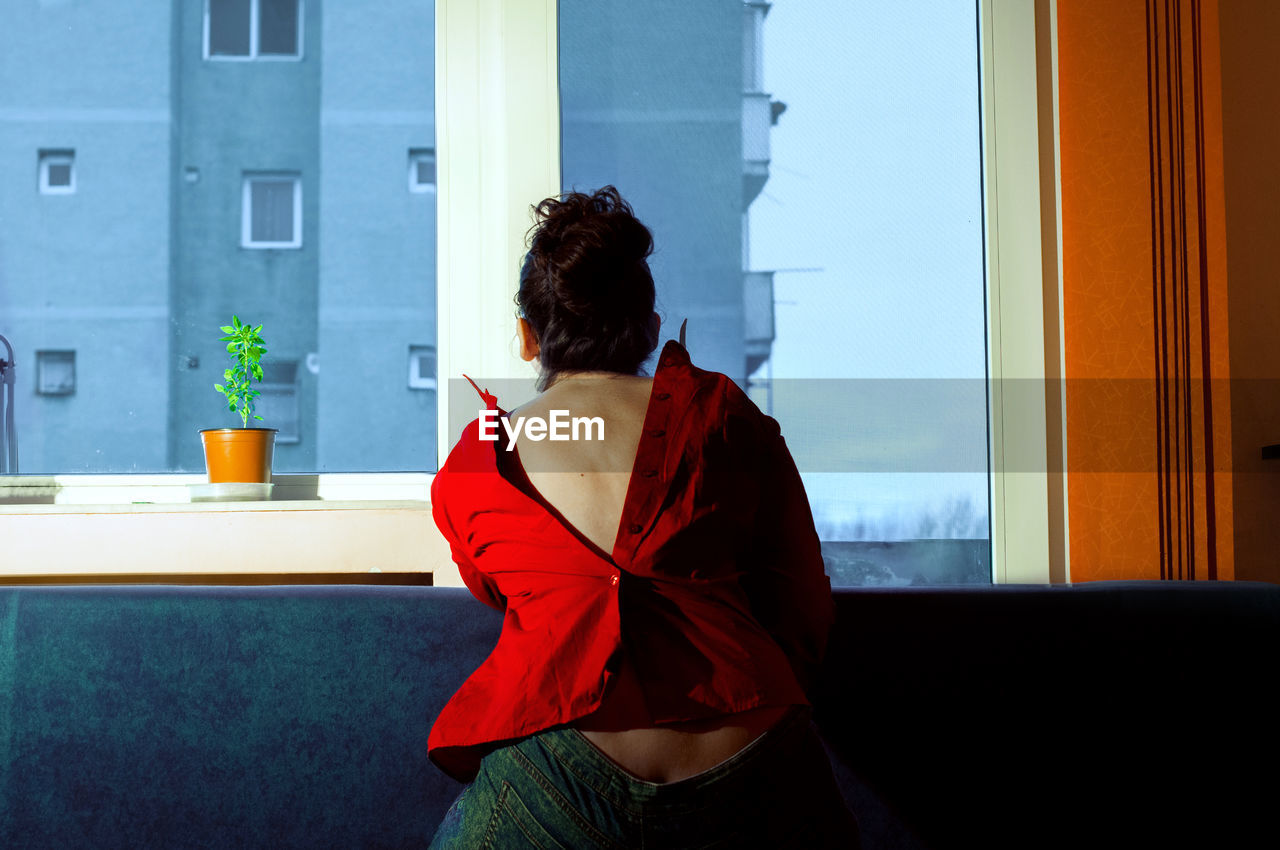 Rear view of woman wearing button down shirt while standing by window at home
