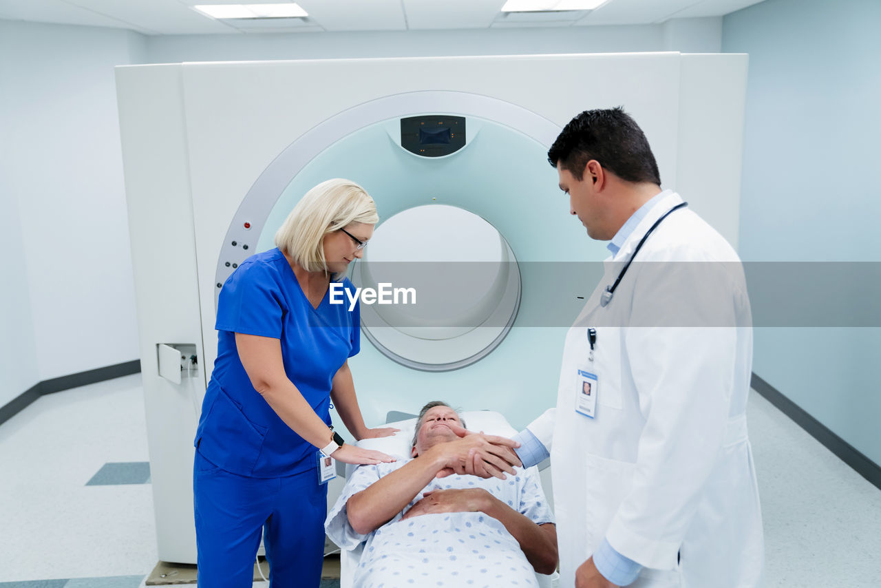 Doctor shaking hands with patient lying by nurse for mri scan in examination room