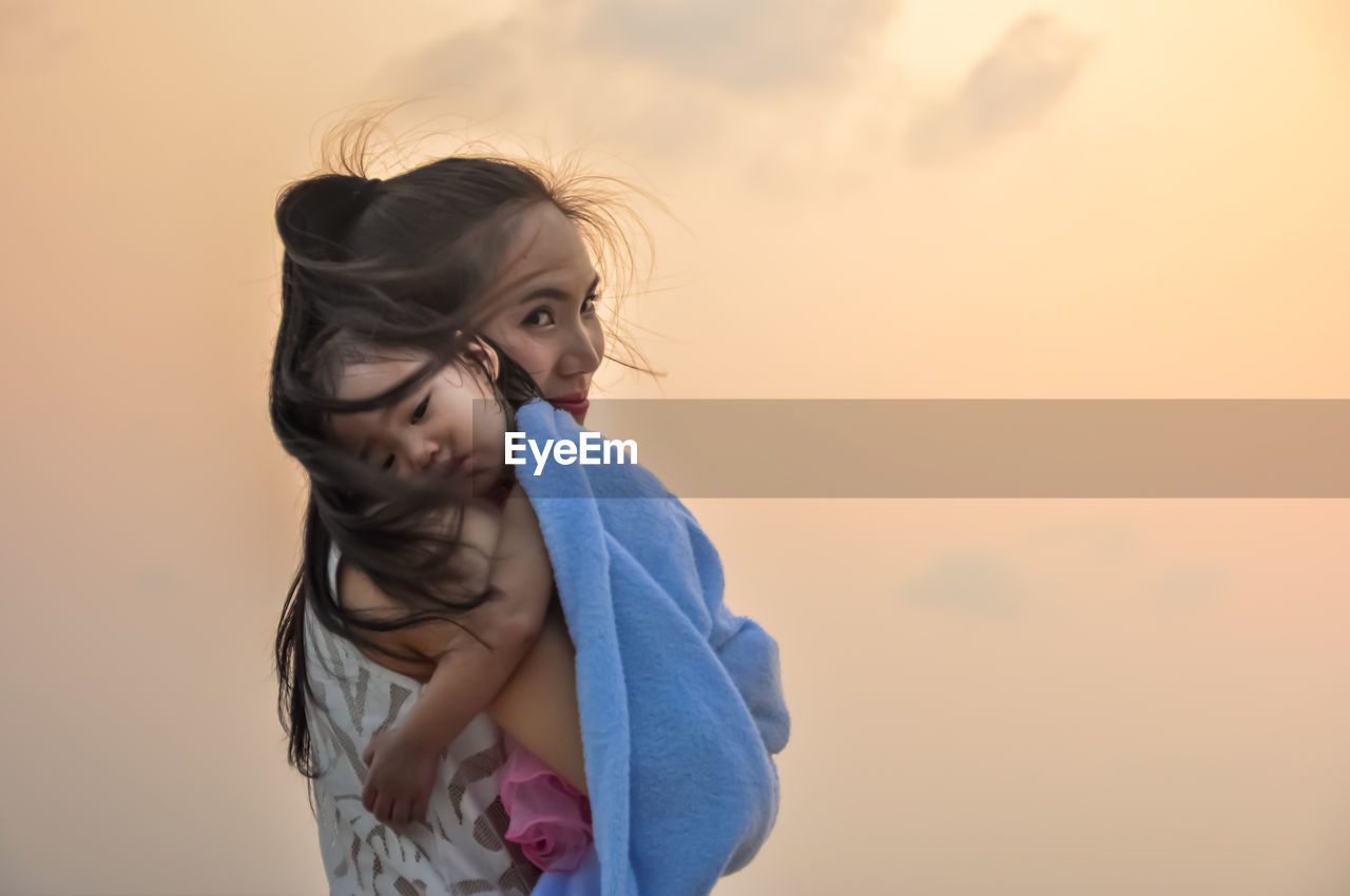 Portrait of mother carrying daughter against orange sky