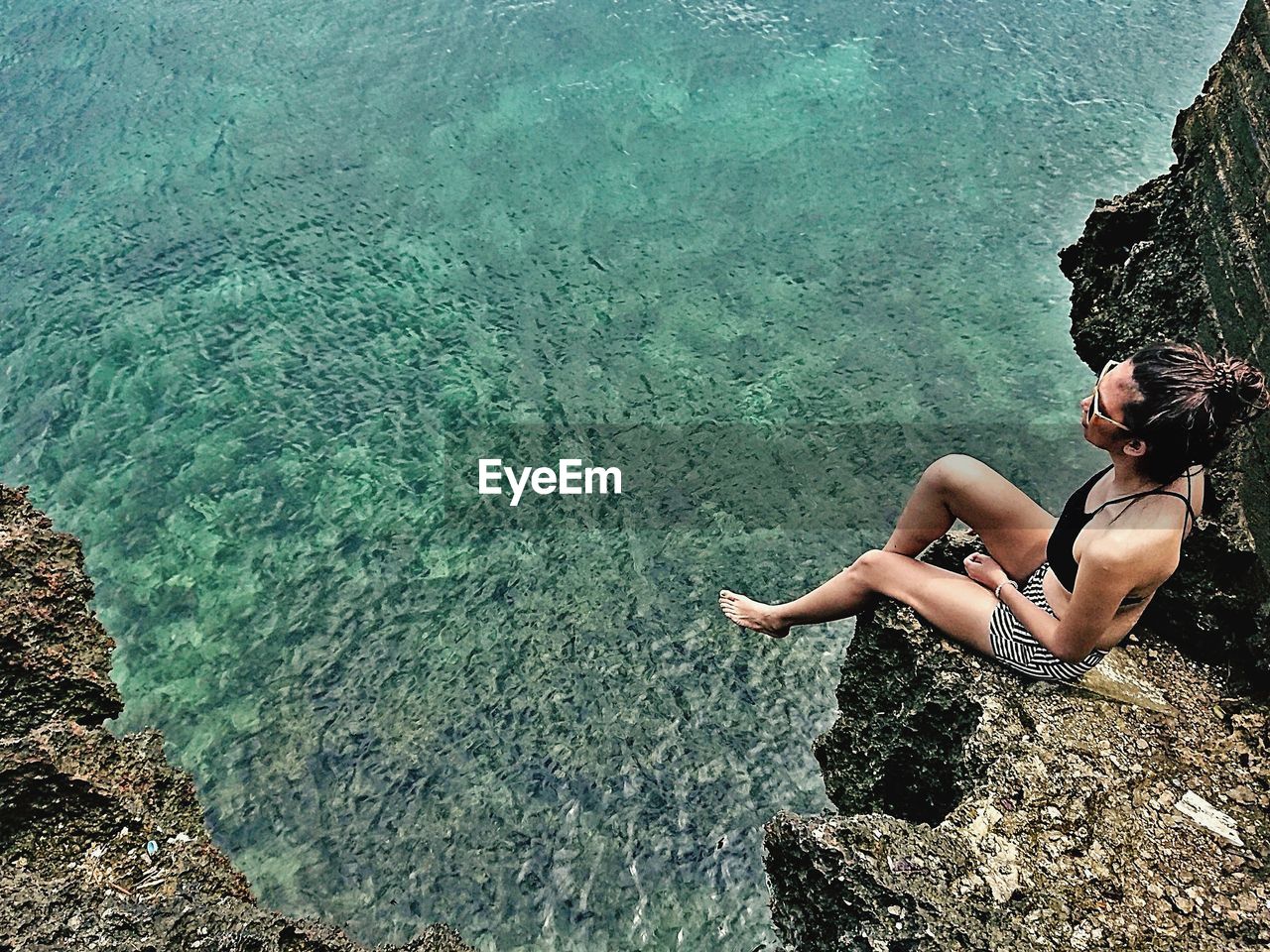 High angle view of woman sitting on cliff against sea