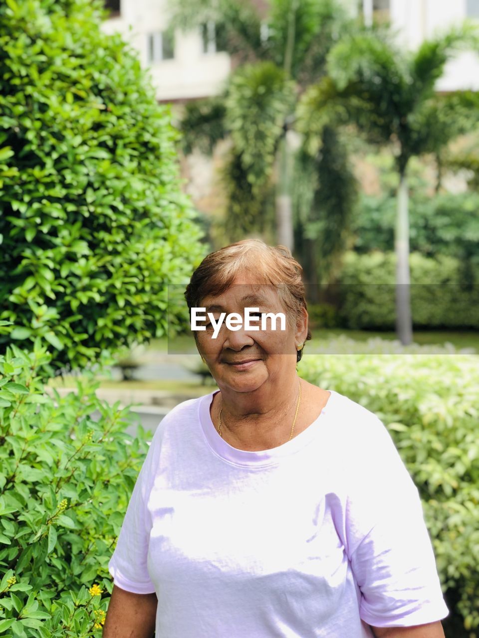 Portrait of old woman standing outdoors against green plants 