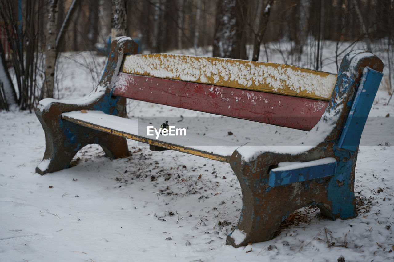 EMPTY BENCH IN SNOW COVERED FIELD