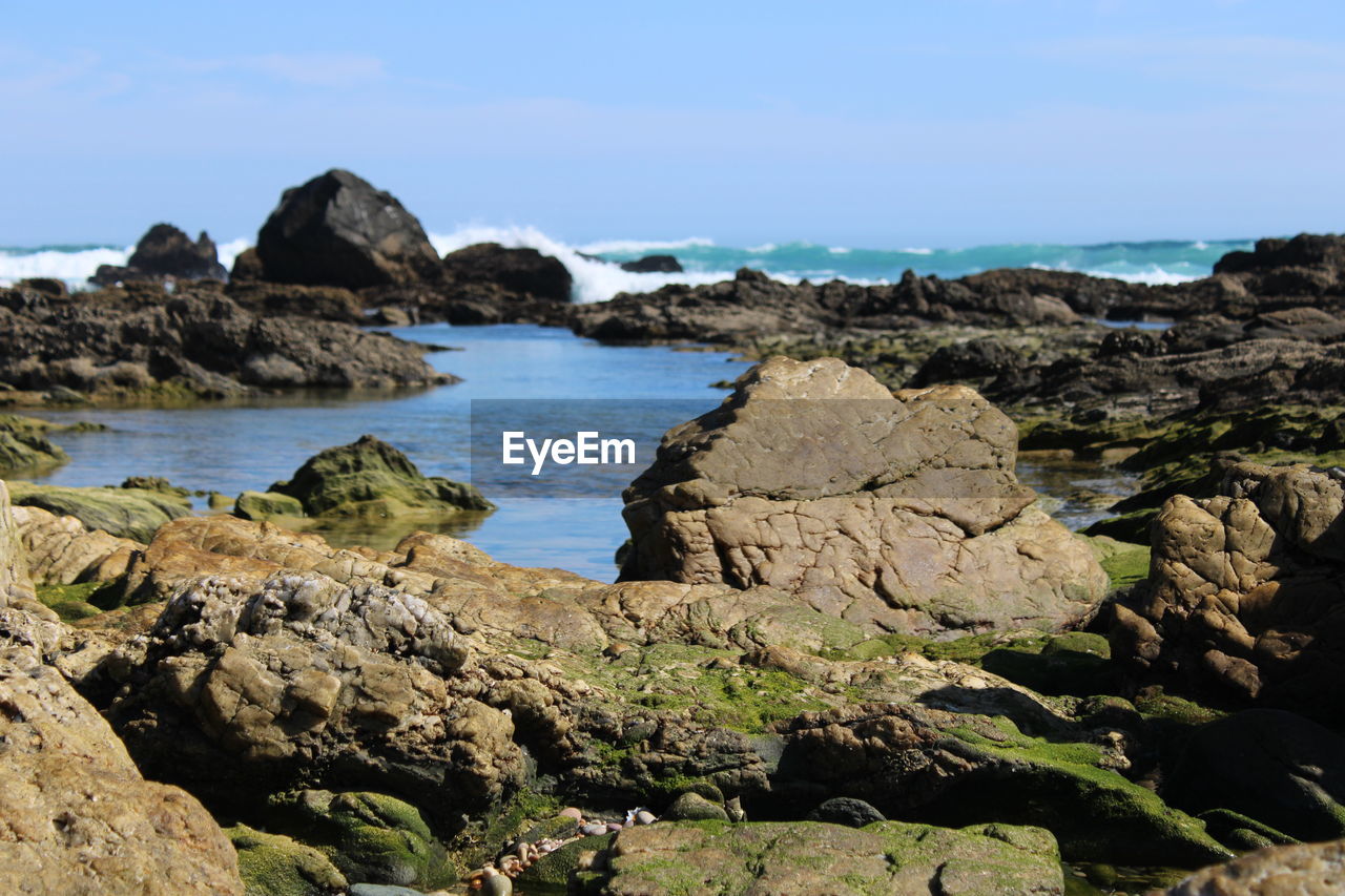 Scenic view of rocks on shore, waves breaking in the background 