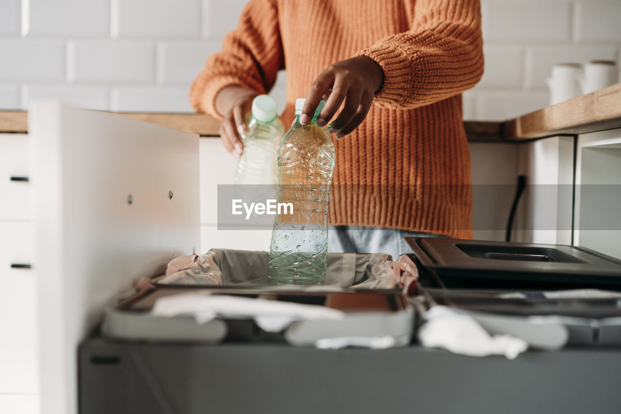 Hands of girl putting plastic bottles in recycling bin at home