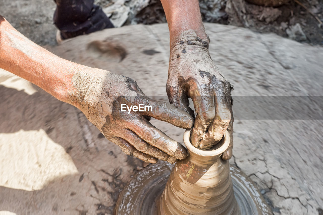 Cropped hands of male potter making pot on field