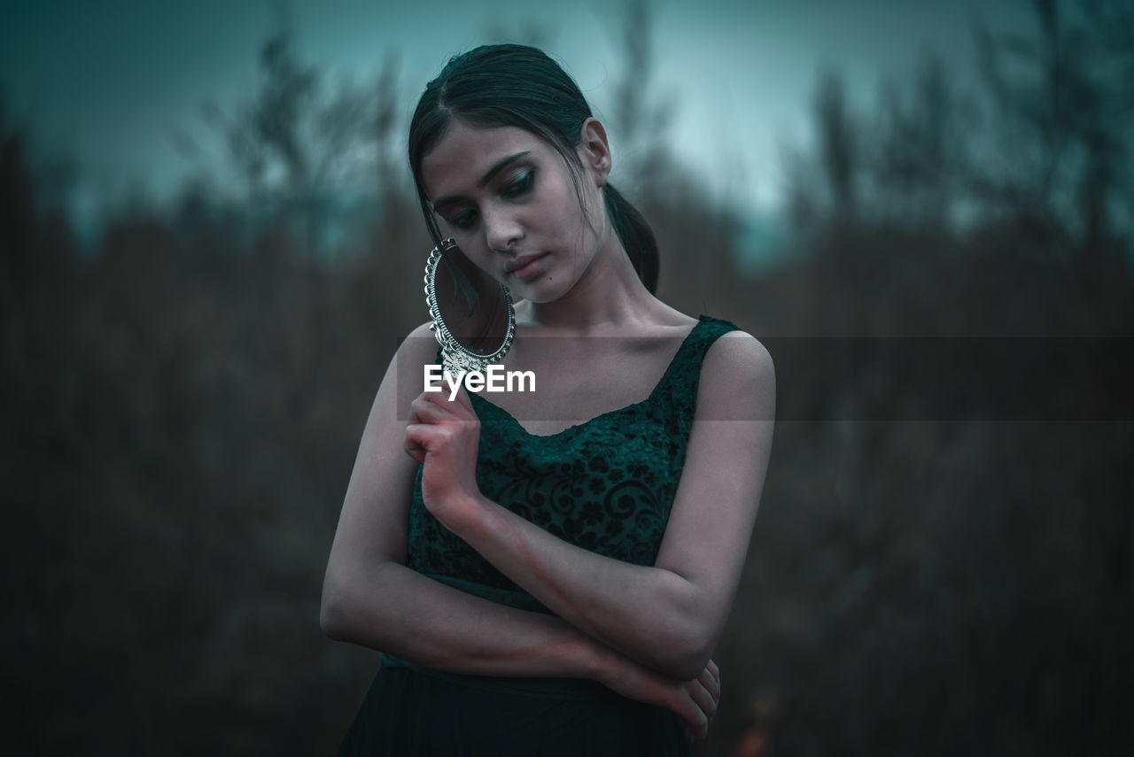 PORTRAIT OF BEAUTIFUL WOMAN STANDING AGAINST BLURRED BACKGROUND