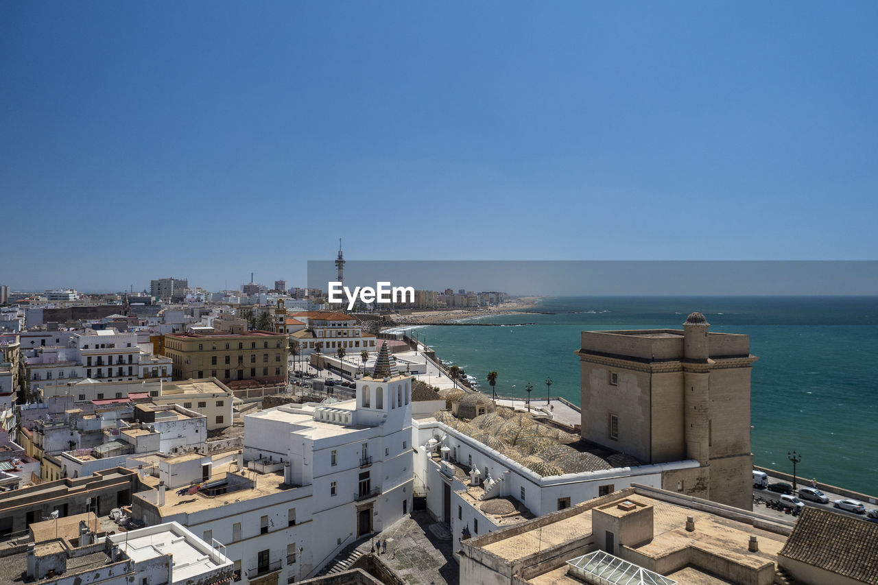 Buildings by sea against clear blue sky