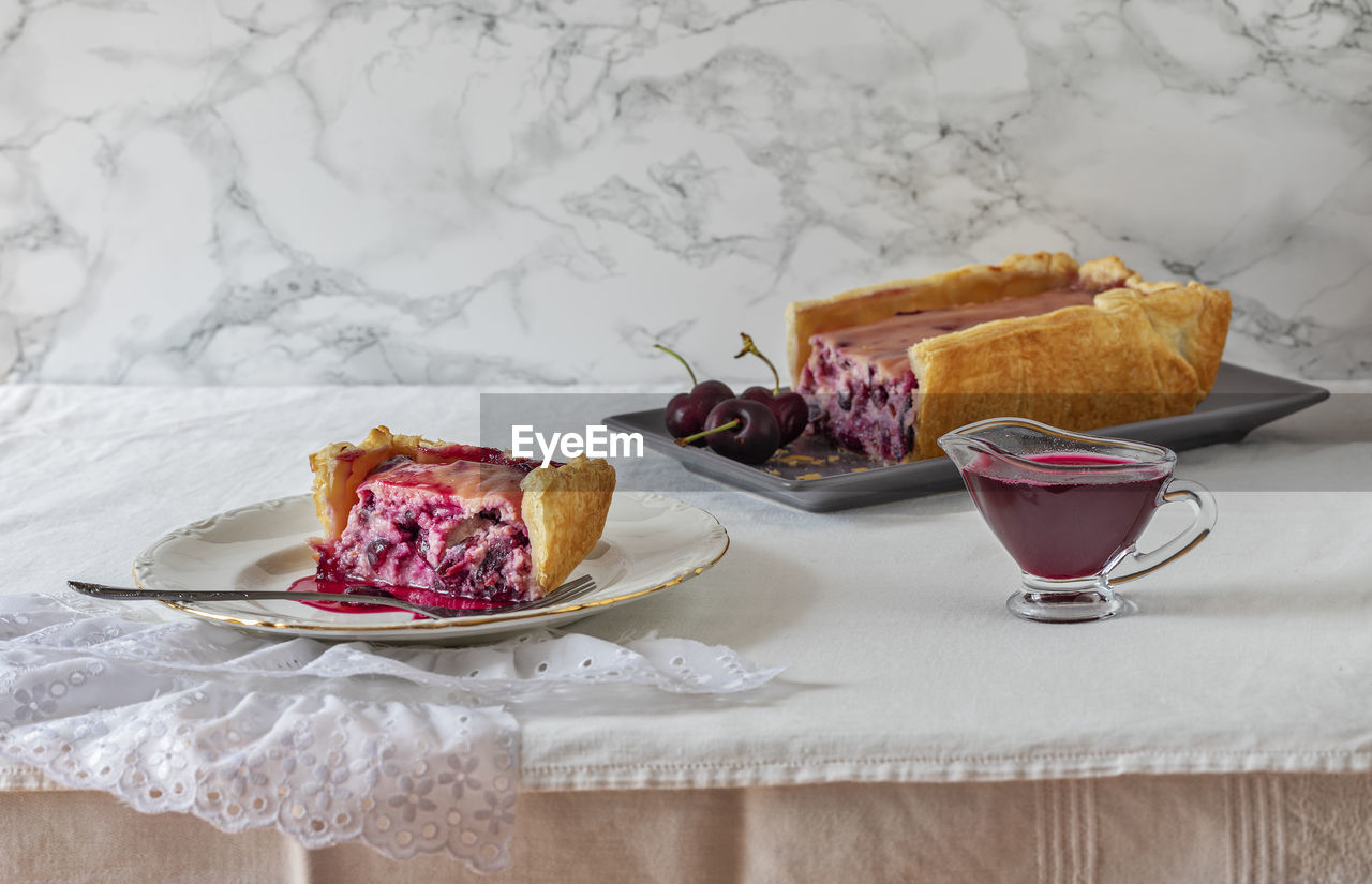 A slice of ricotta cheese and cherry cake. at the side glass jug with cherry syrup. 