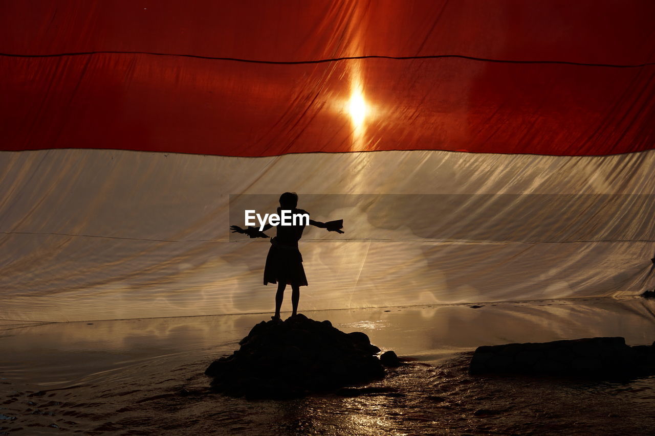 Rear view of silhouette man standing on rock at sea