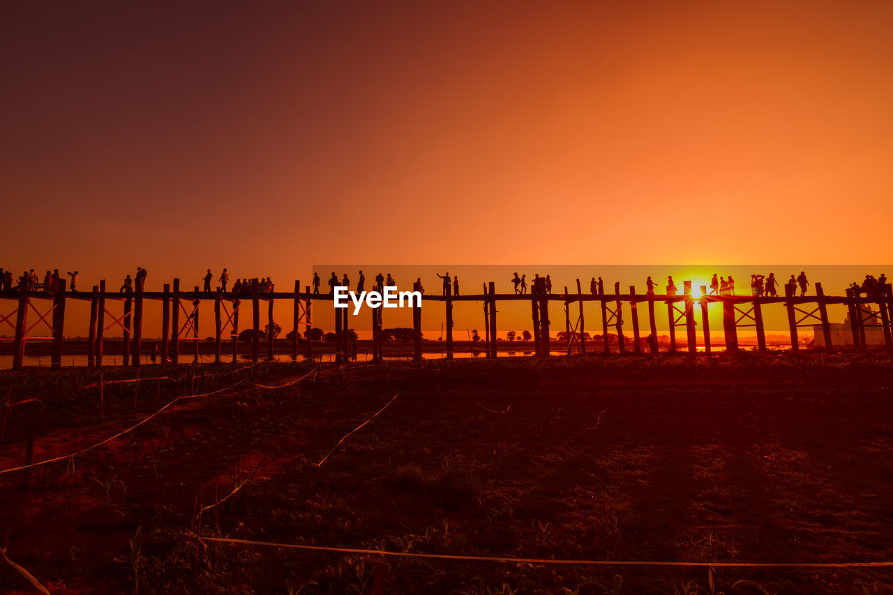 Silhouette of locals walking on ubein bridge against orange sky