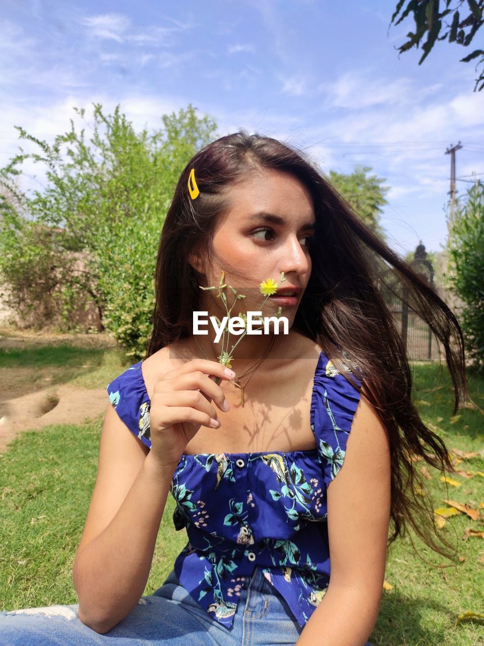 Young woman holding flower against sky