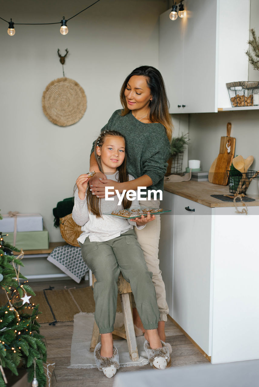 Stylish mom and daughter in homemade clothes eat christmas cookies in the kitchen