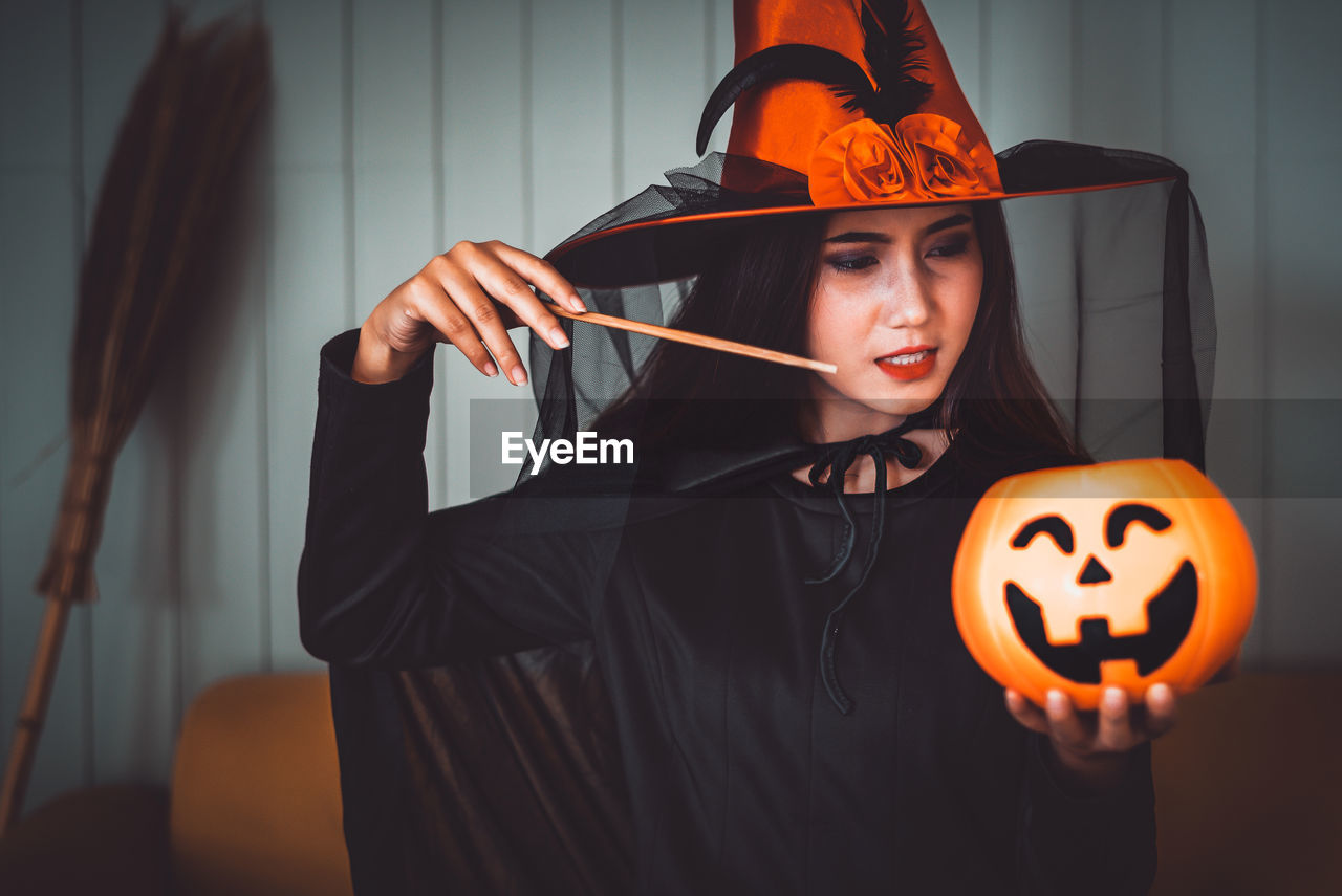 Woman wearing witch costume holding jack o lantern during halloween