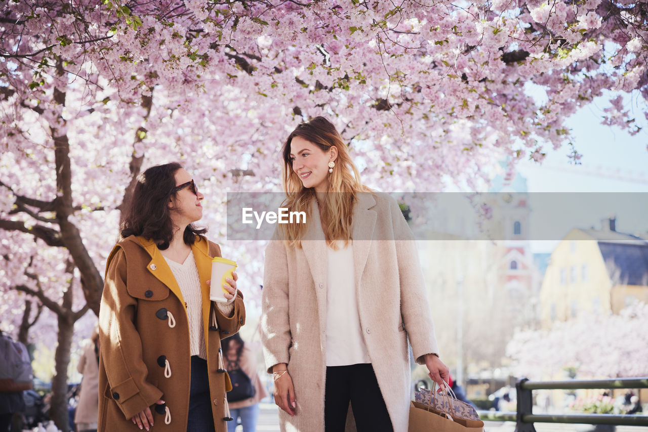 Smiling young women walking under cherry blossom