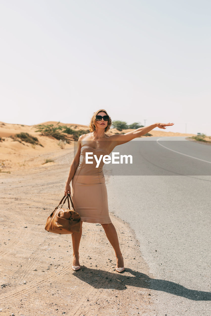 A stylish woman catches a car on a deserted road on a sunny day