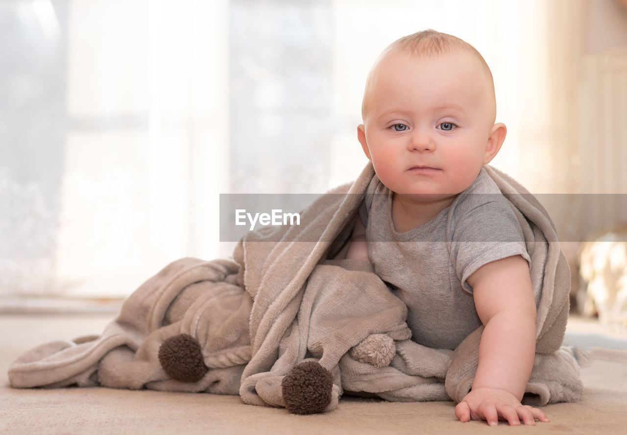 Portrait of cute baby boy with blanket sitting at home