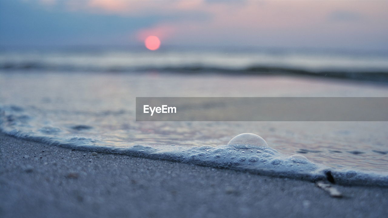 Close-up of beach against sky during sunset