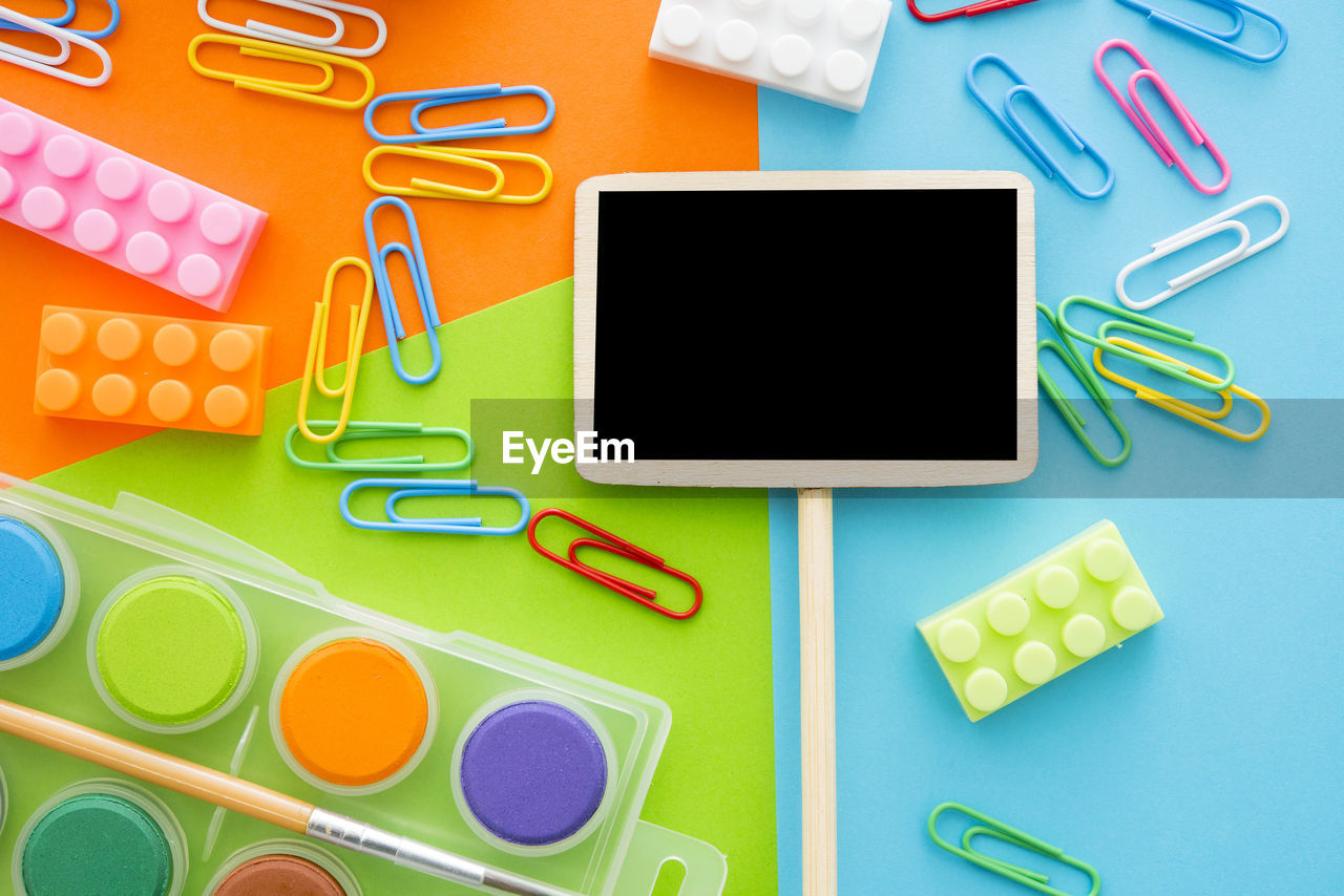 High angle view of blank blackboard with colorful paper clips and toy blocks on colored background