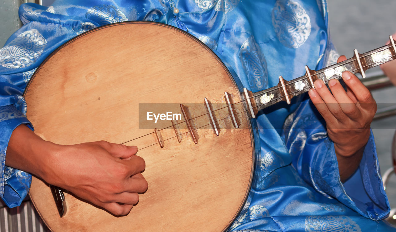 Midsection of person playing traditional guitar