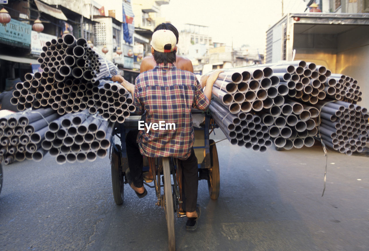 Rear view of people in tricycle while carrying pipes on street