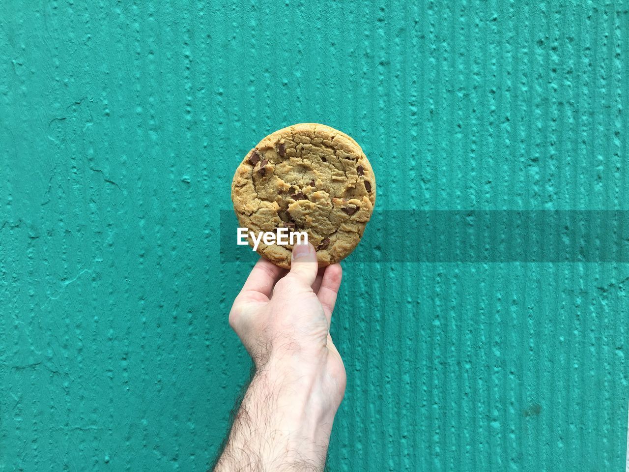 Cropped image of hand holding cookie against wall