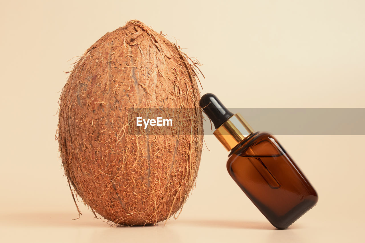 Fresh coconut and glass bottle of cosmetic oil on beige background. organic cosmetic concept