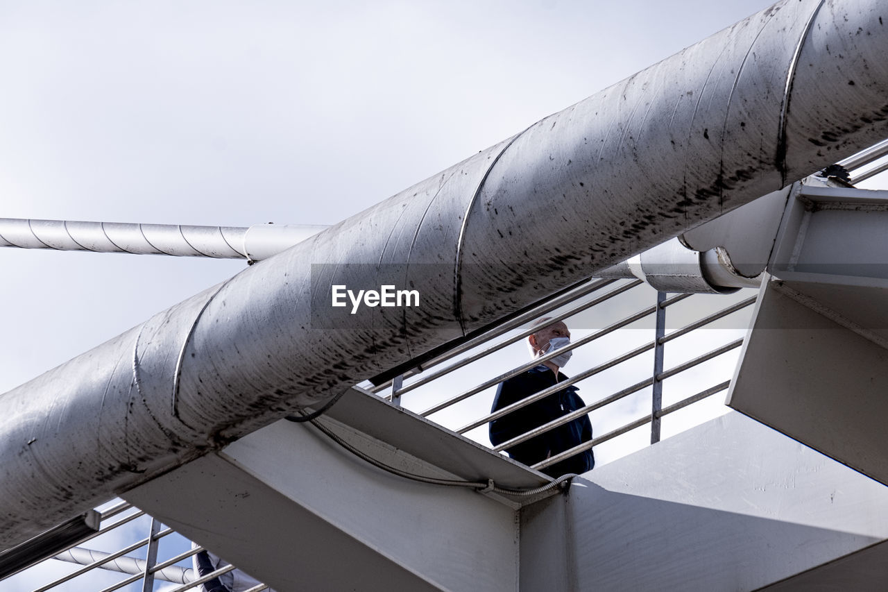 Low angle view of man standing by railing against sky