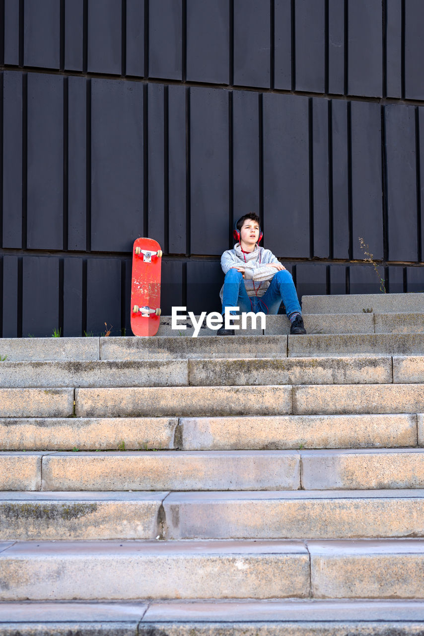 Teenager with headphones listening music while sitting on staircase.