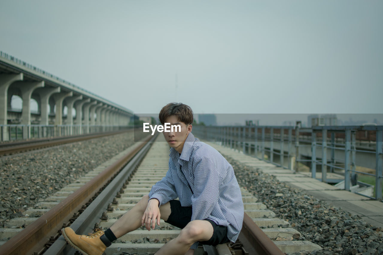 Man sitting on railroad track against clear sky