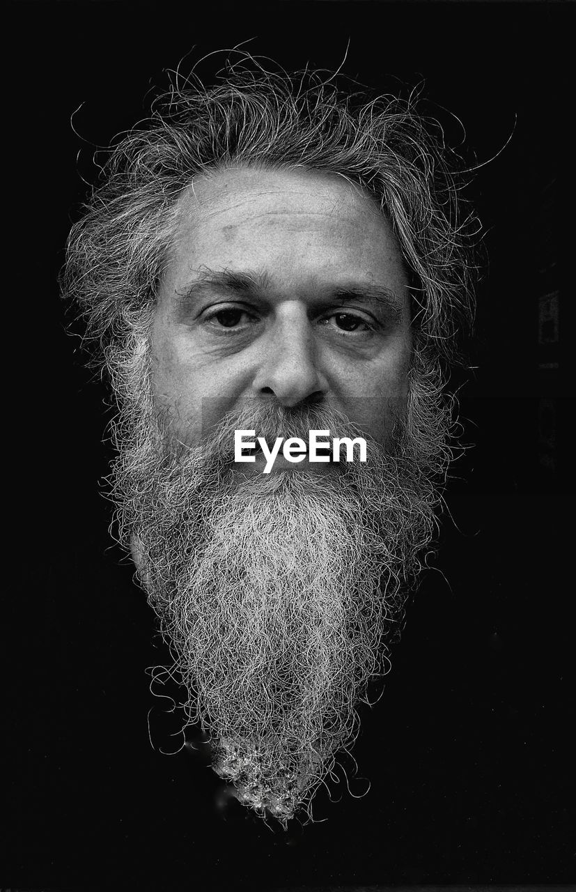 Close-up portrait of senior man with beard against black background