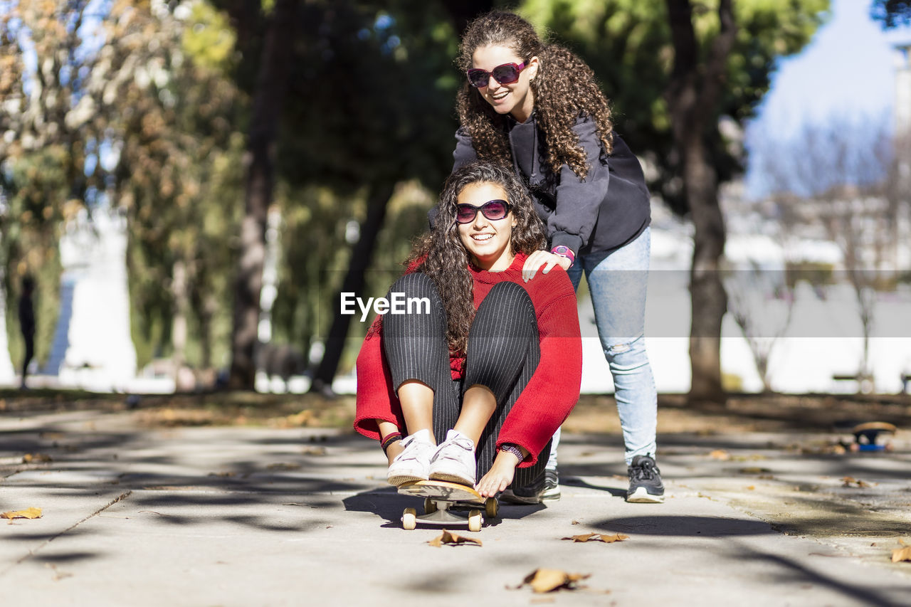 Playful female friends enjoying with skateboard outdoors