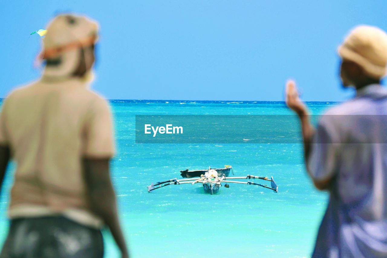 REAR VIEW OF PEOPLE IN SEA AGAINST CLEAR SKY