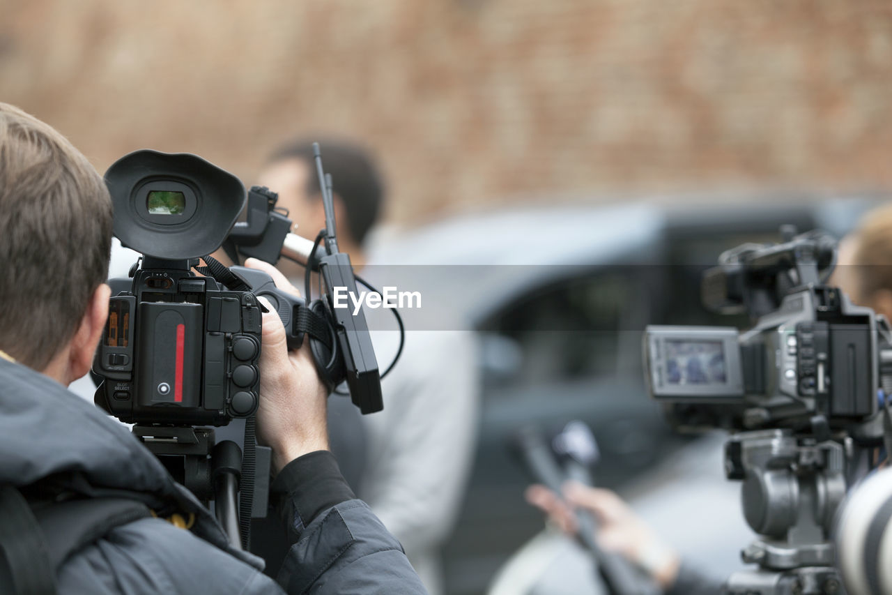 Rear view of journalist filming media event with television camera