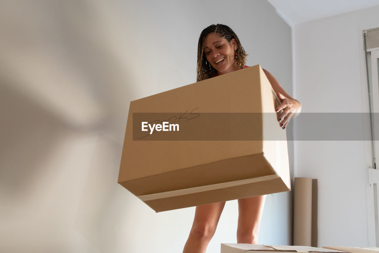 Happy woman holding cardboard box against wall