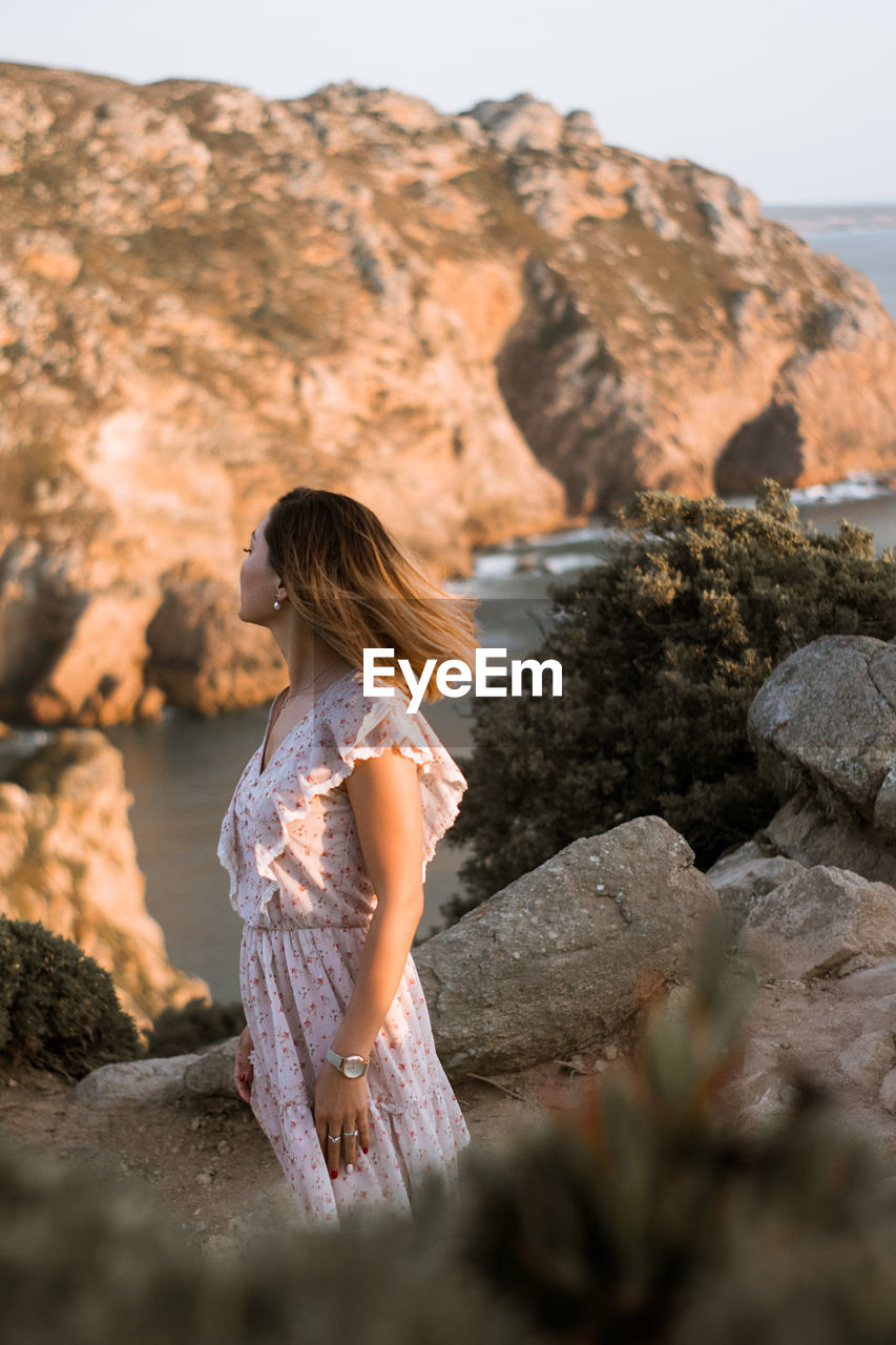 Side view of woman looking away while standing at rock formation