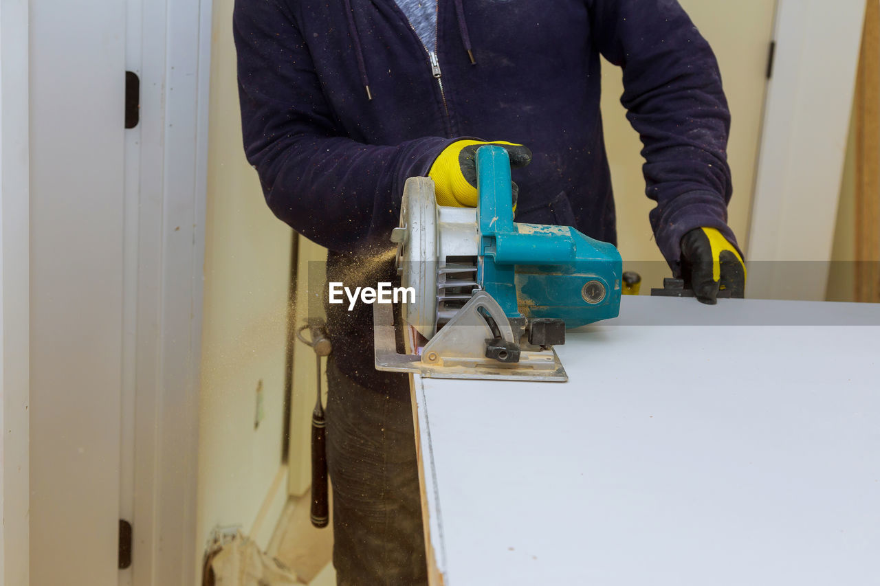 Midsection of carpenter using machinery on wood