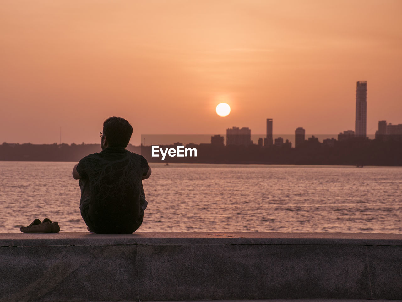 Rear view of silhouette man sitting by river against sky