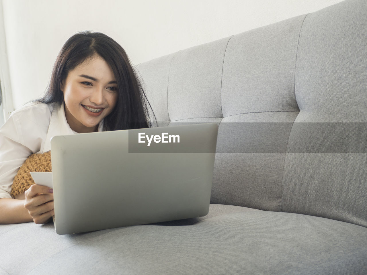 Smiling woman using laptop while lying on sofa at home