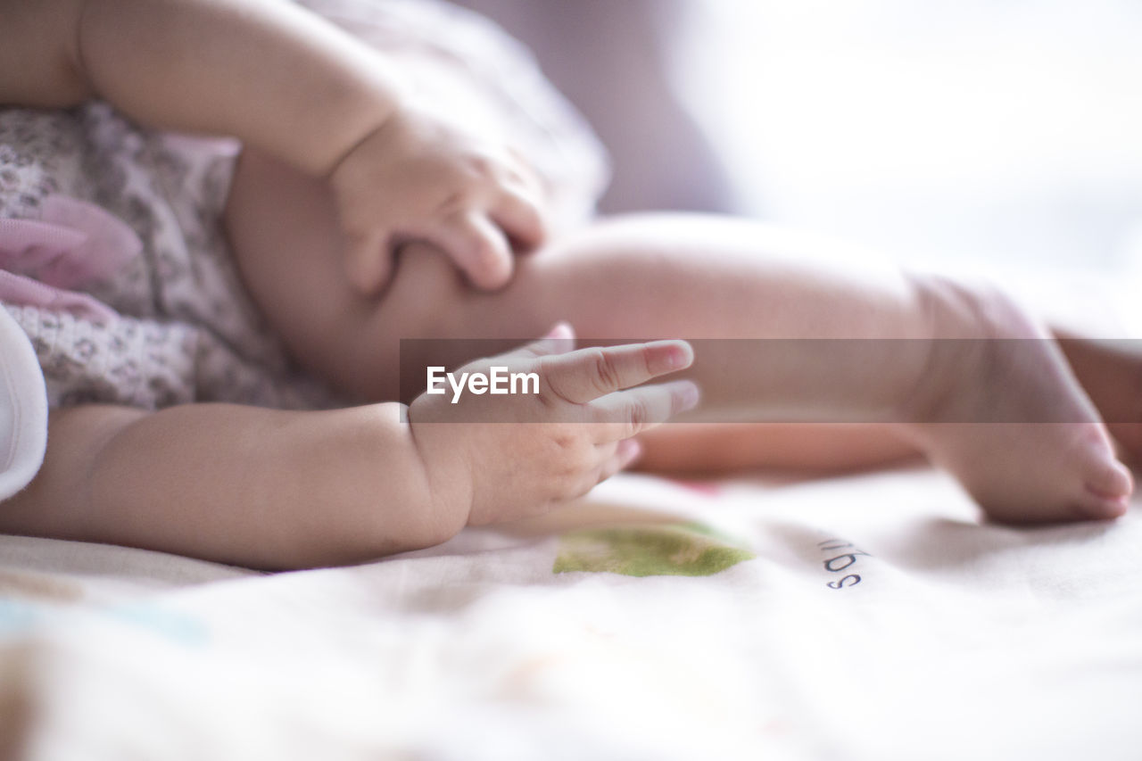 Low section of baby relaxing on bed at home