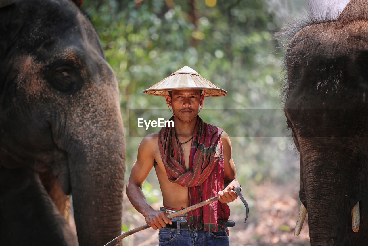 Man wearing conical hat standing by elephant outdoors