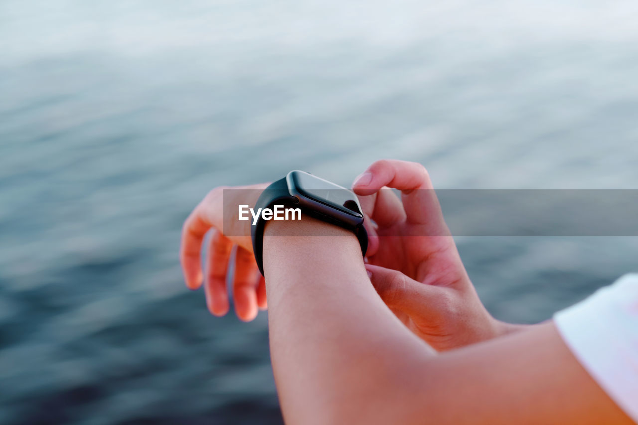 Cropped hand of person wearing smart watch against sea