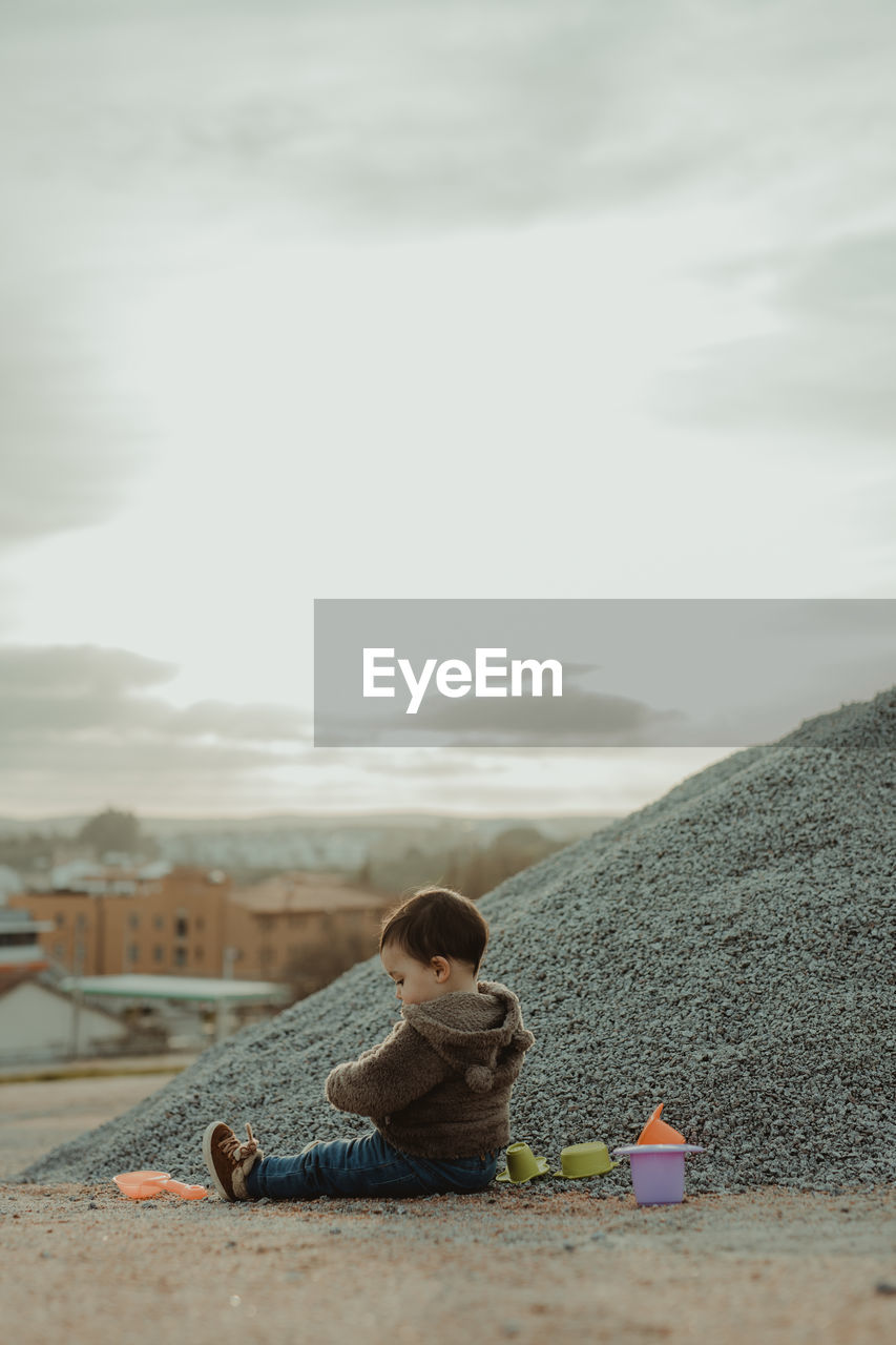 Child sitting on land against sky