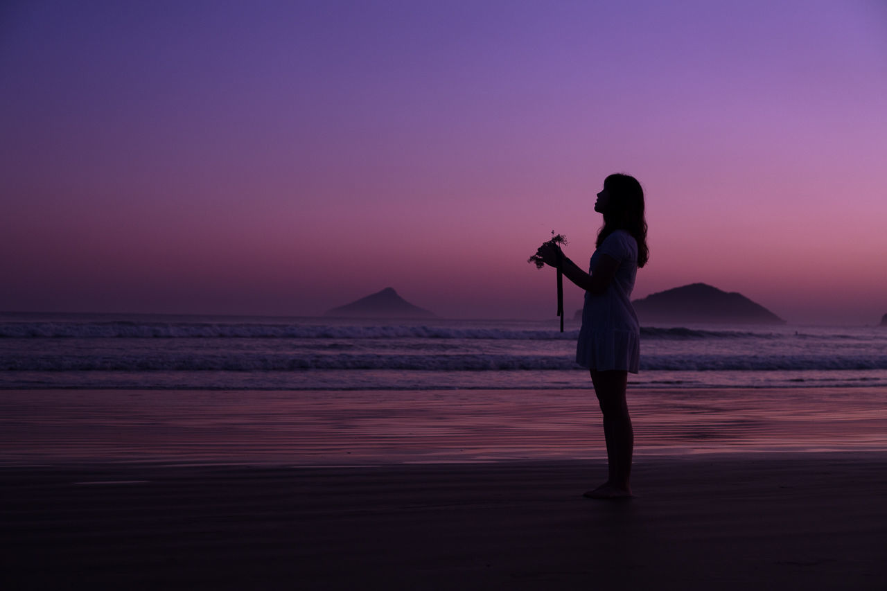 Woman standing on sea shore against clear sky at dusk