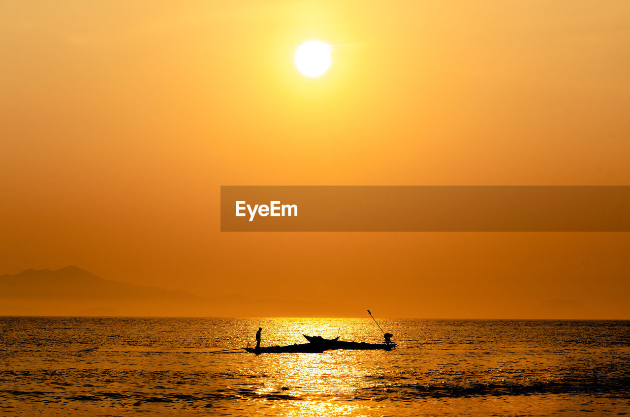 Silhouette boat in sea against orange sky