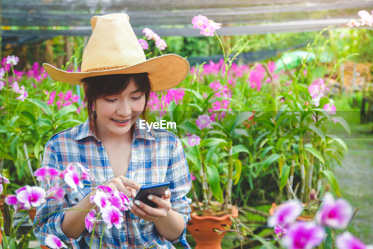 young woman using mobile phone while standing by plants