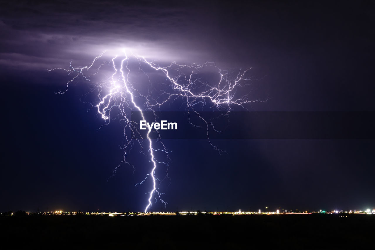 A lightning strike from a monsoon thunderstorm illuminates the night sky over phoenix, arizona.