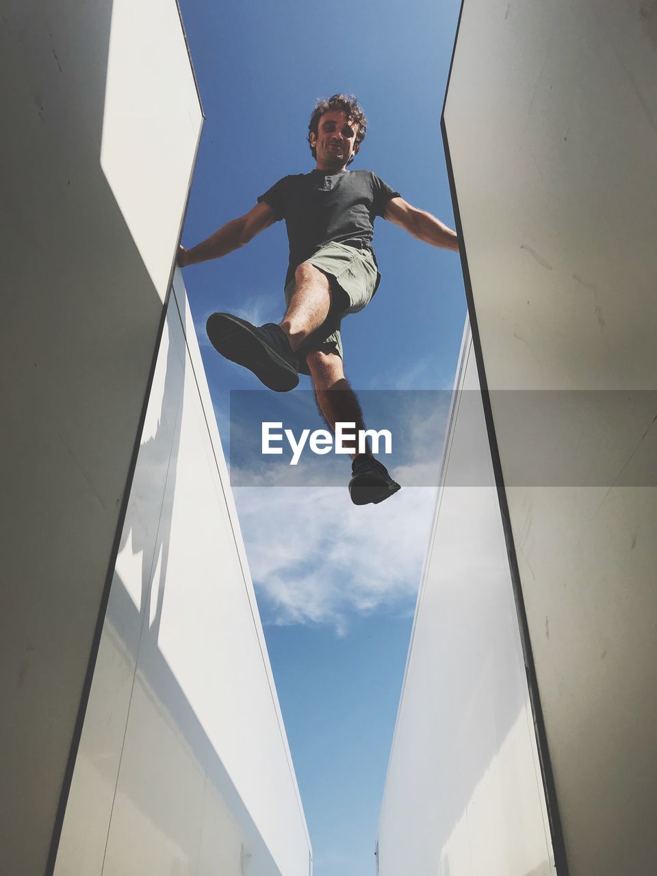 Low angle view of man jumping amidst buildings against sky